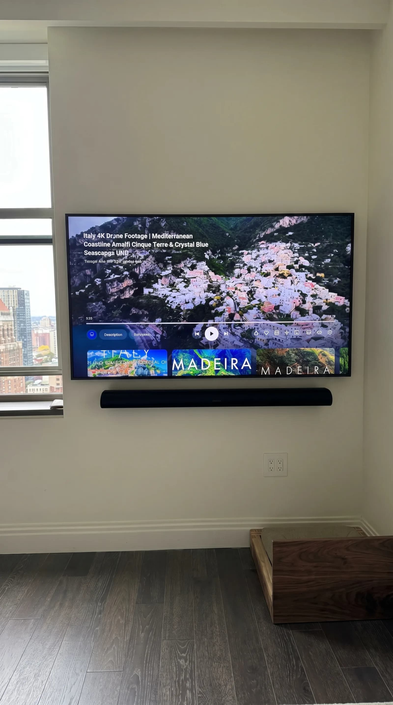 Wall-mounted TV with a soundbar beside a city-view window