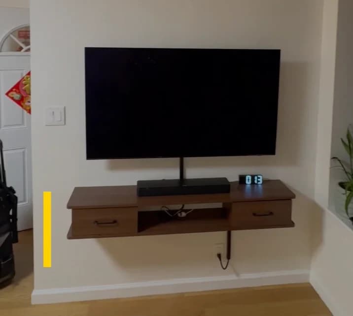 Flat-screen TV mounted above a walnut floating media stand with drawers in an NYC apartment living room