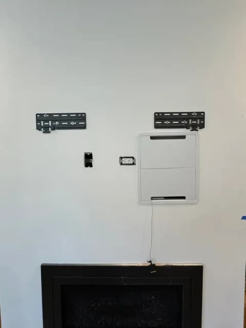 Closed recessed AV box and black mount plates installed above a black fireplace.