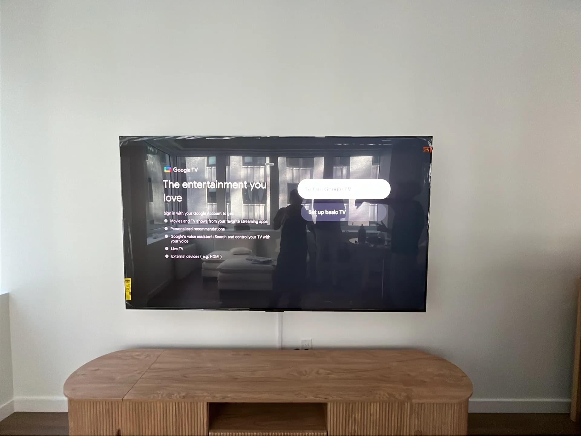 Wider view of the same wall-mounted TV showing the Google TV setup screen above the wood credenza.