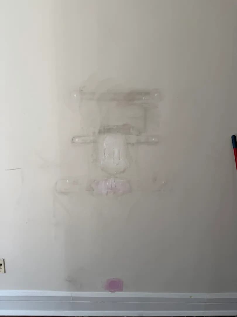 A wall shows several patched spots of spackle compound covering old mount holes, not yet painted, with a light switch below a