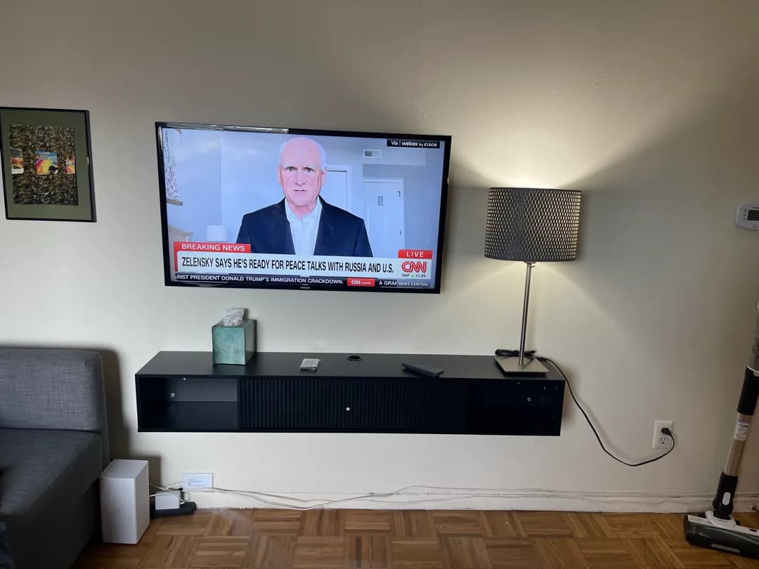 A wall-mounted TV above a newly installed dark floating console, with a lamp and framed art nearby.