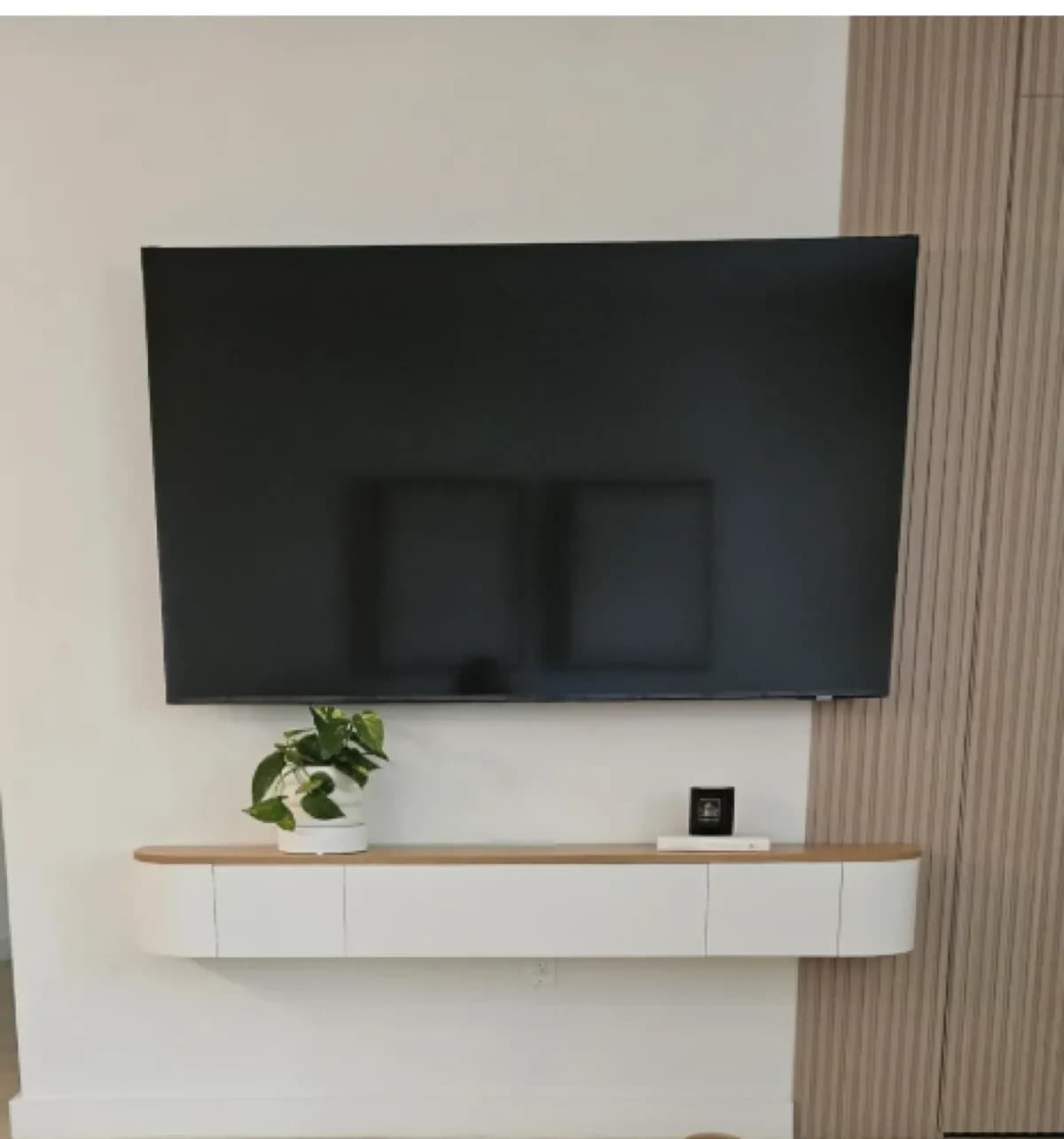 Large TV wall-mounted above a custom white floating stand with wood top in a modern living room