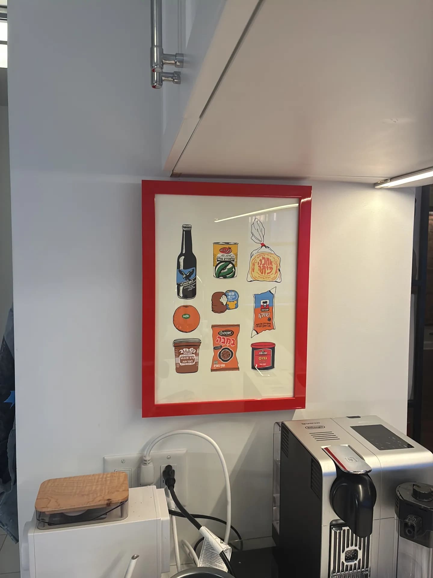 A red-framed print hangs on a white wall above a coffee machine and kettle.