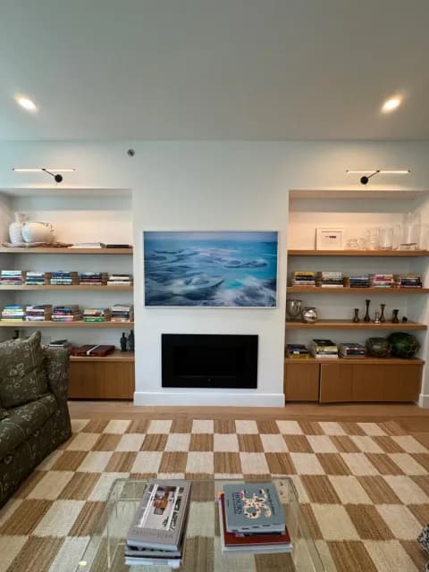 Finished living room with a Frame TV above the fireplace between furnished built-in shelves.