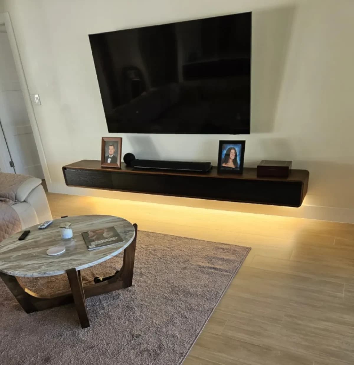TV wall-mounted above a dark floating media stand with warm LED underlight glow in a modern living room