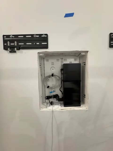 Open recessed AV box holding a device and cables below Frame TV mount plates.