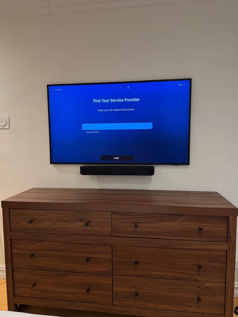A wall-mounted television and soundbar above a walnut dresser