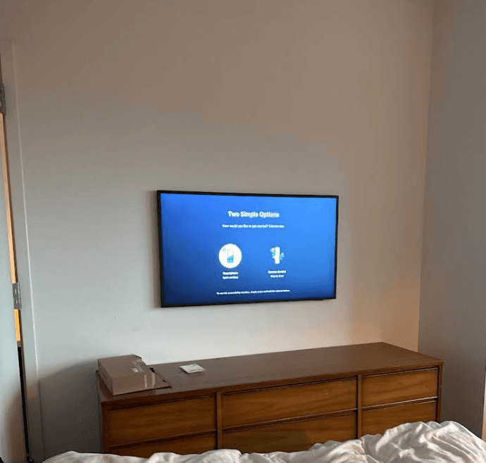 Samsung Frame TV mounted above a wooden dresser in an NYC bedroom with One Connect cable hidden in the wall