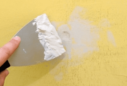 Putty knife patching anchor holes on a yellow wall after large item dismounting
