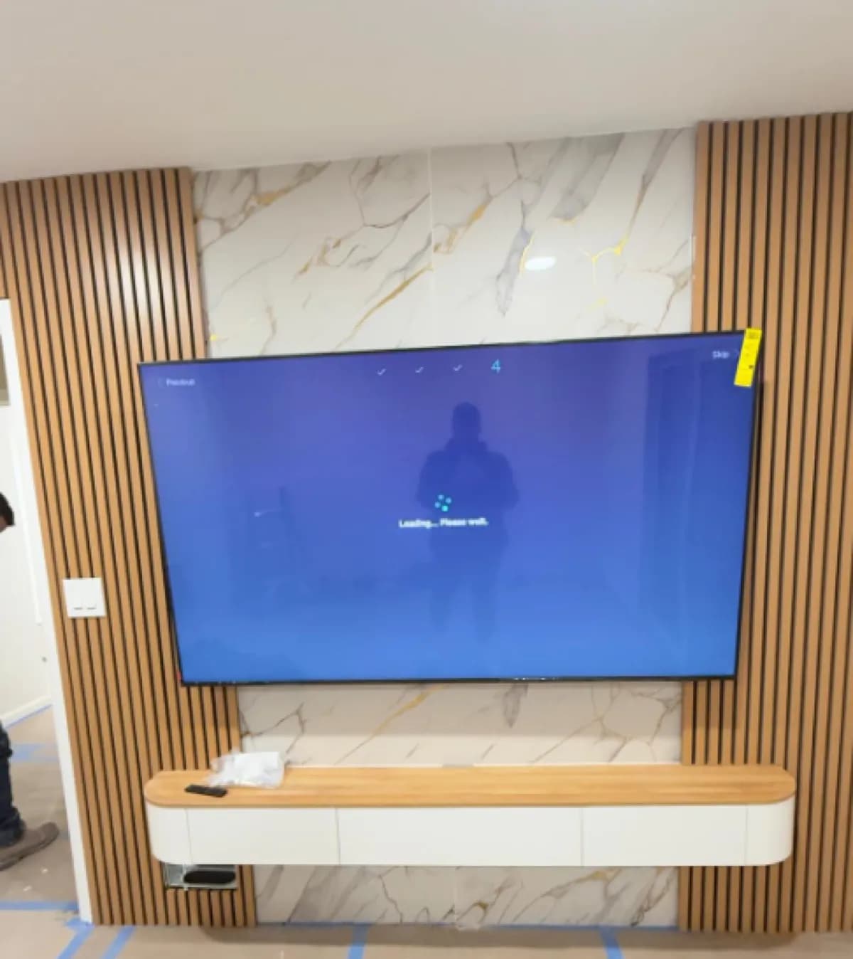 TV mounted on a marble and wood-slat feature wall above a floating cabinet in a modern living room