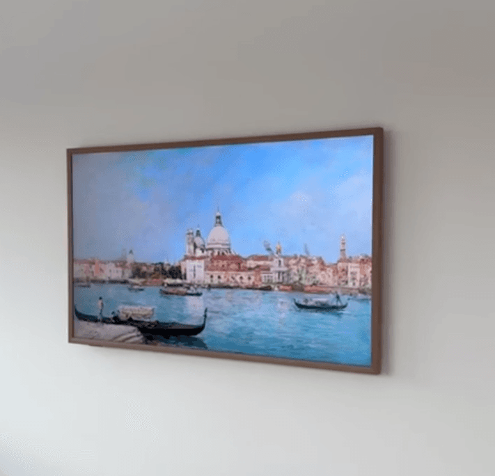 Samsung Frame TV mounted flush like artwork in a wood bezel displaying a Venice canvas scene