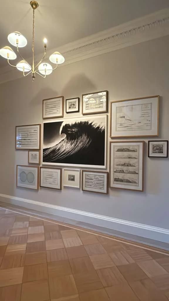 Gallery wall of small framed art and documents mounted in a curated arrangement under a chandelier