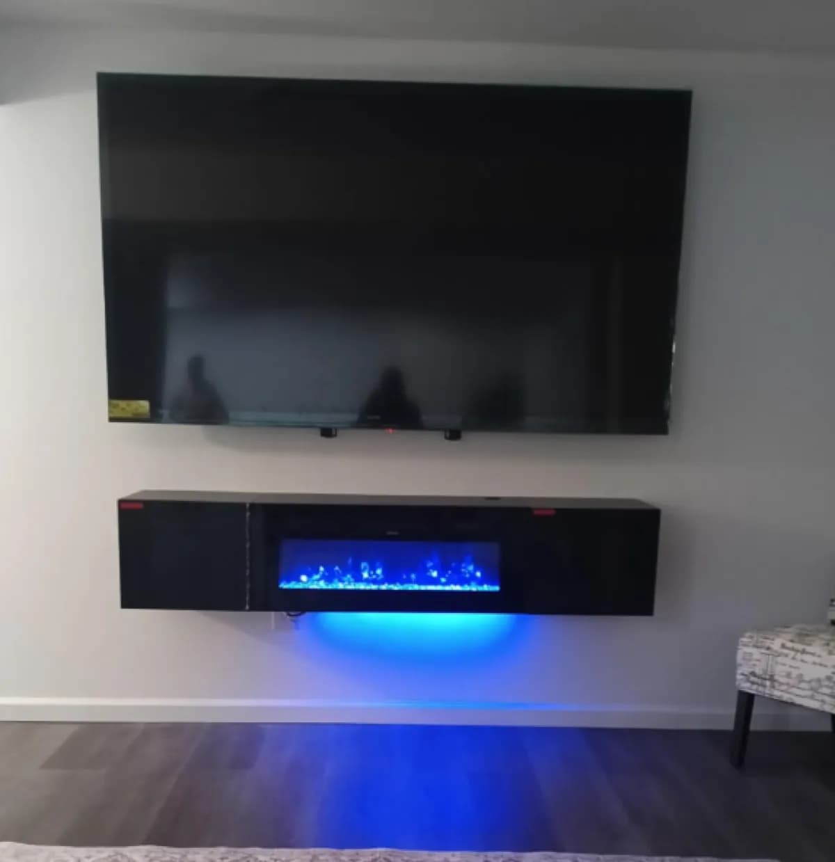 Large TV wall-mounted above a floating electric fireplace insert glowing blue in a bedroom