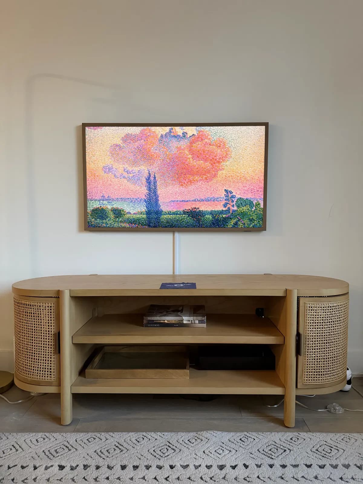 Framed TV wall-mounted above a rattan media console with cables concealed behind the wall