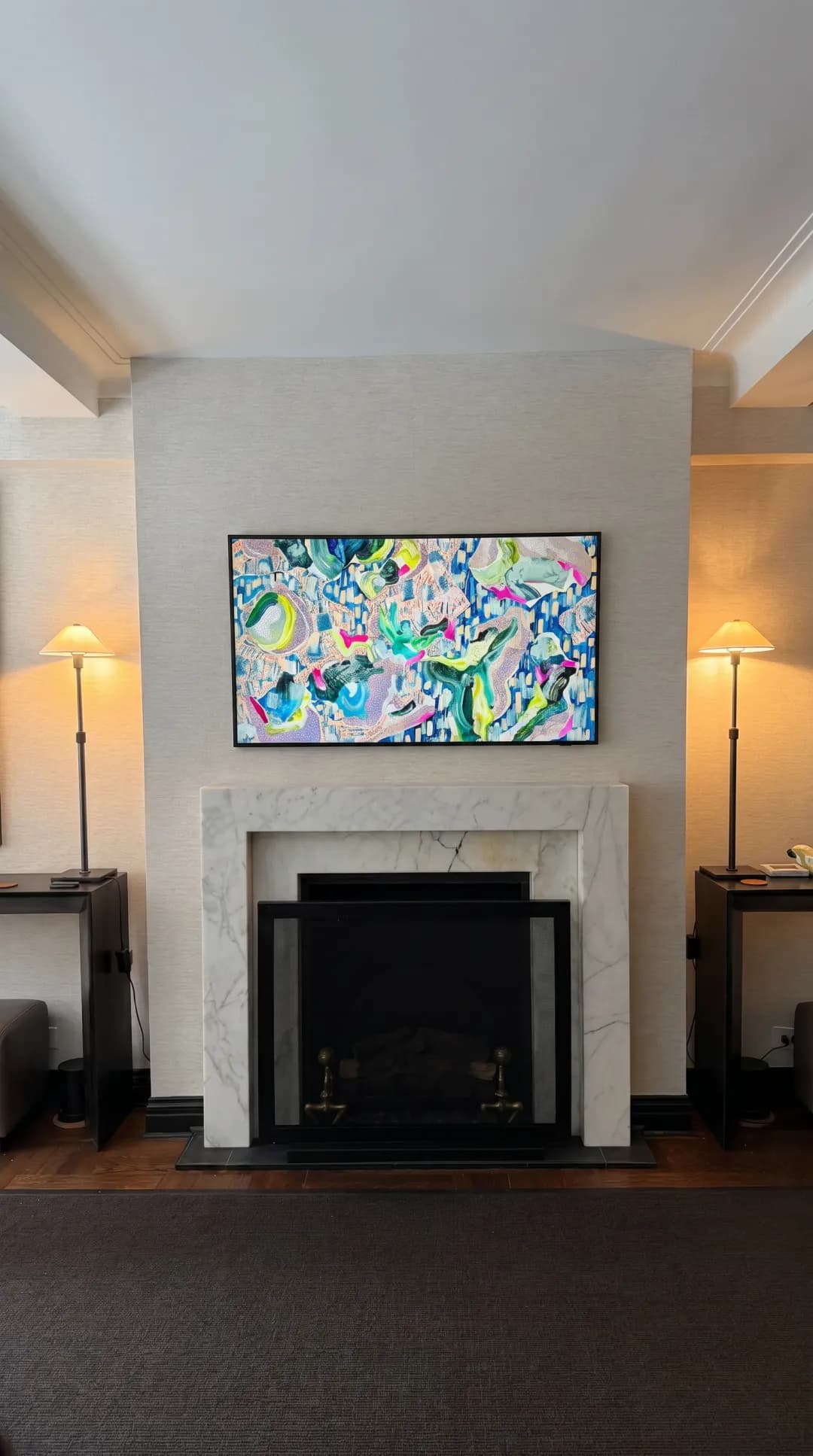 TV mounted above a marble fireplace displaying abstract art in a luxury living room