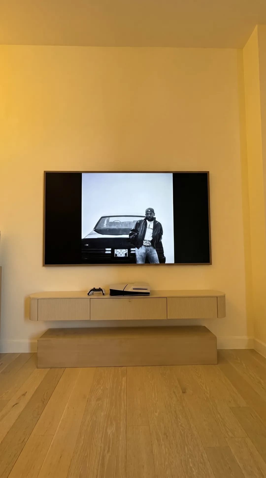 TV wall-mounted above a floating console with a game console in a bright modern room