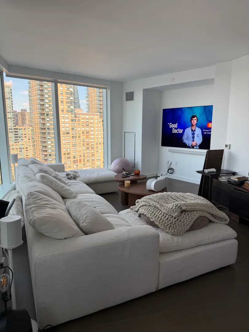 A wide shot of the living room: the sectional sofa, the city skyline through the windows, and the finished TV and soundbar.