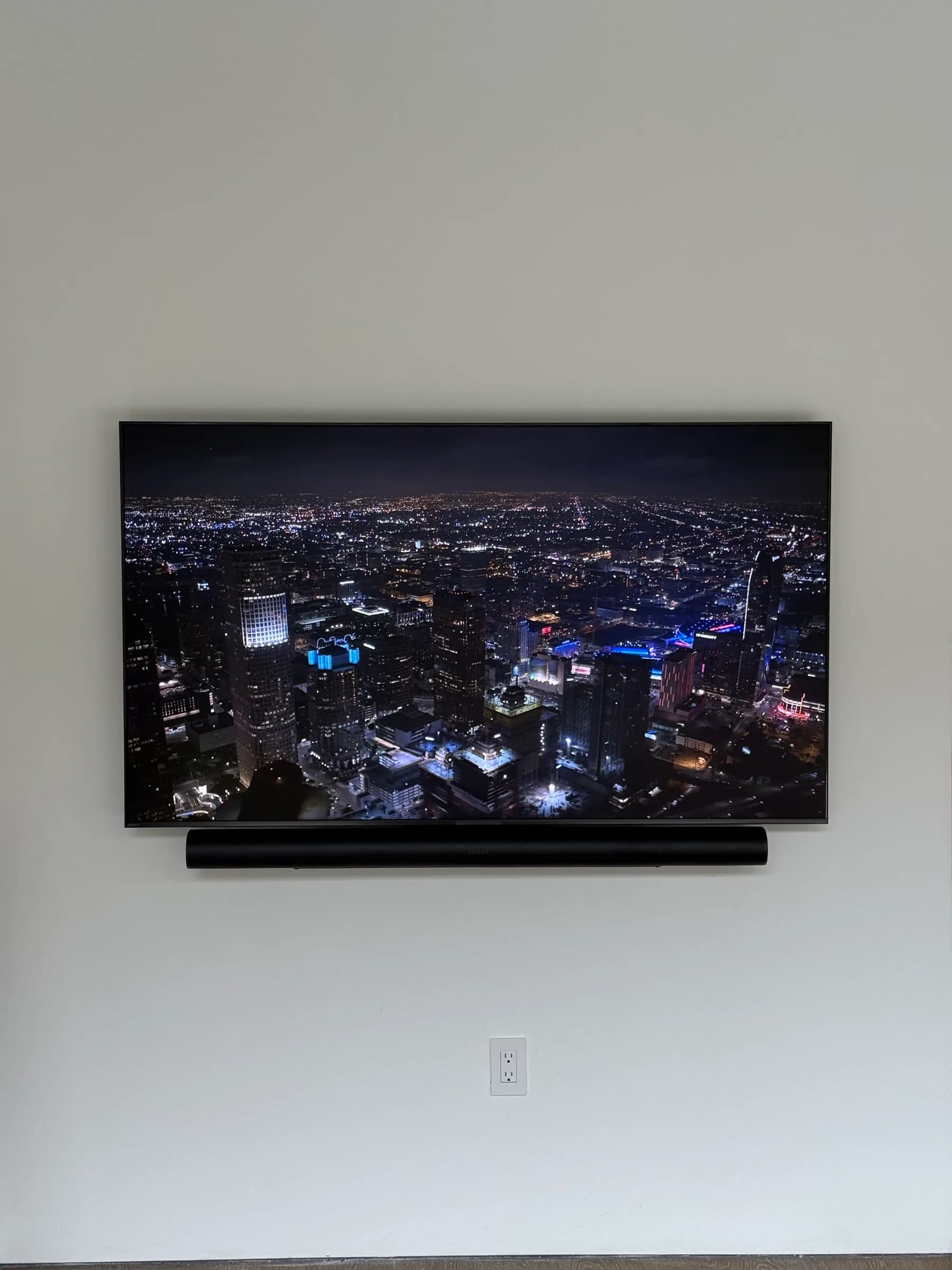 A wall-mounted TV showing a night city skyline, with a soundbar mounted below it