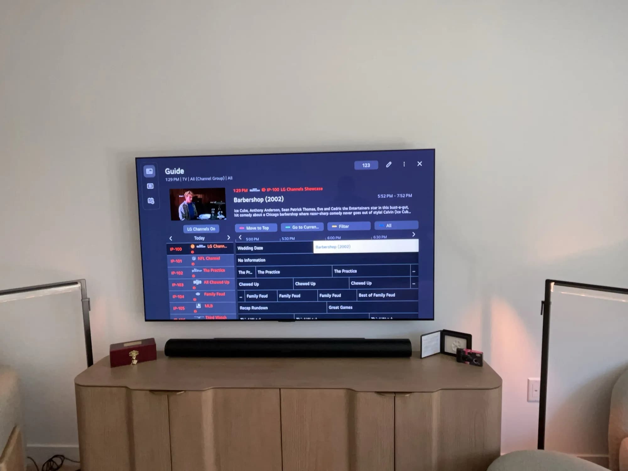 A wall-mounted TV showing a channel guide above a soundbar and media console with decor.