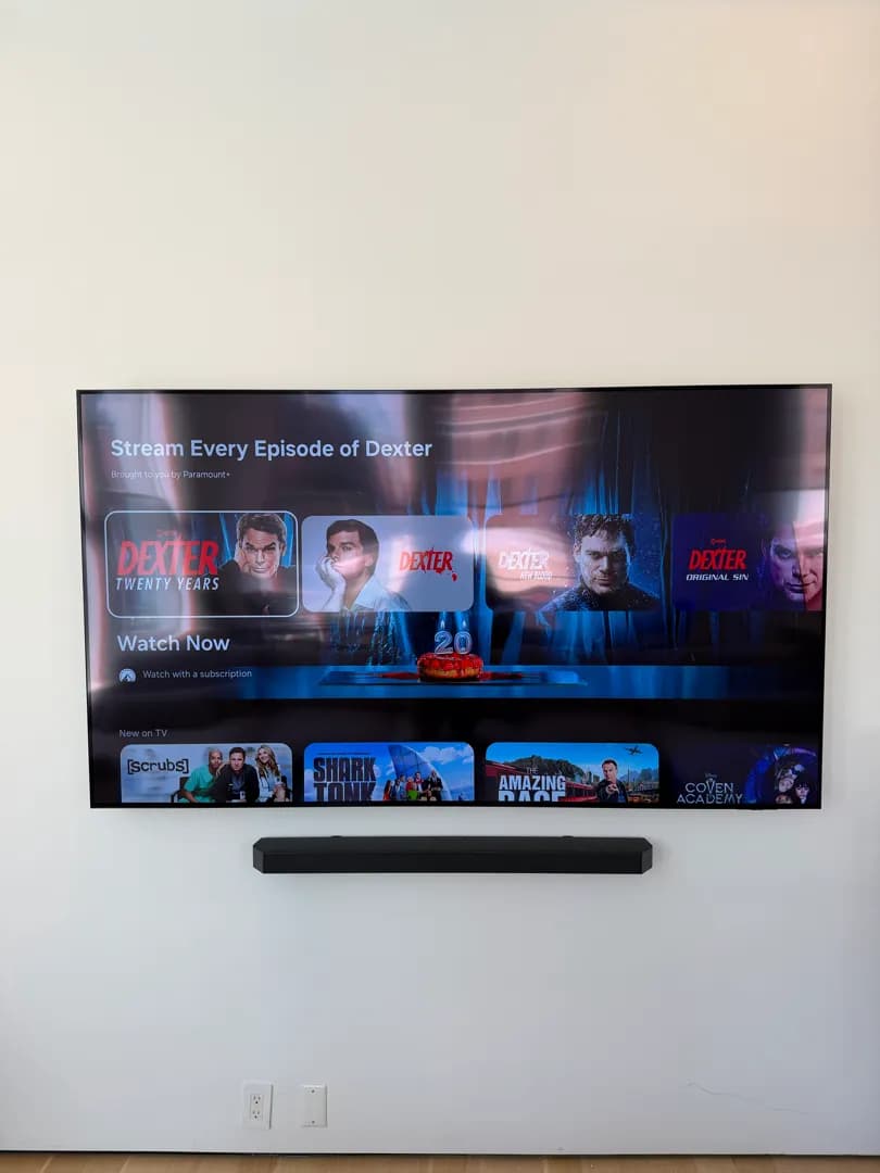 The same large TV and soundbar on the clean white wall, viewed straight on.