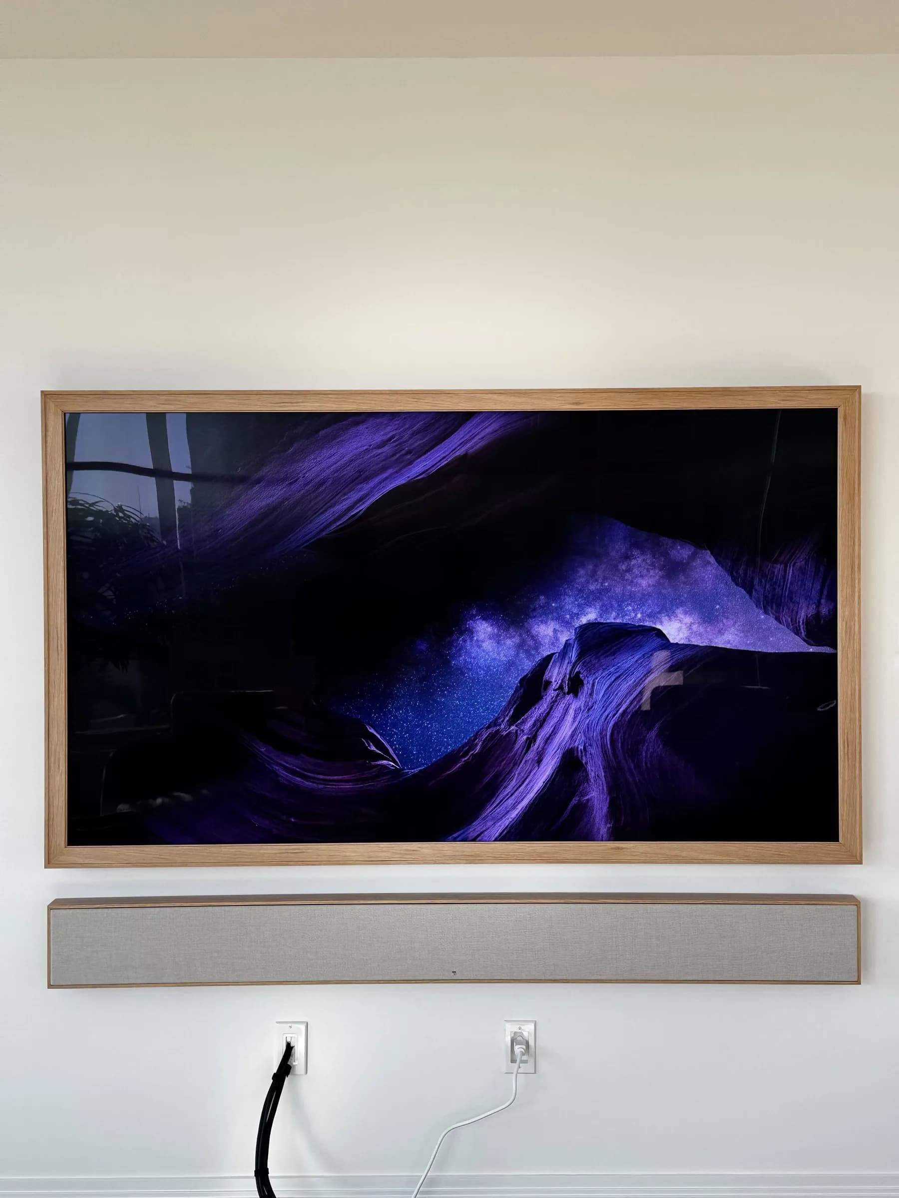 A wood-framed TV in Art Mode showing a purple and blue landscape image, soundbar mounted below.