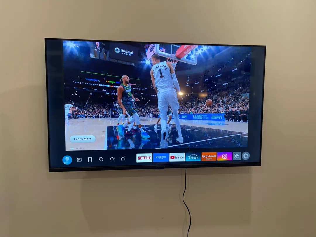 A flat TV hangs on a beige wall playing a basketball game.