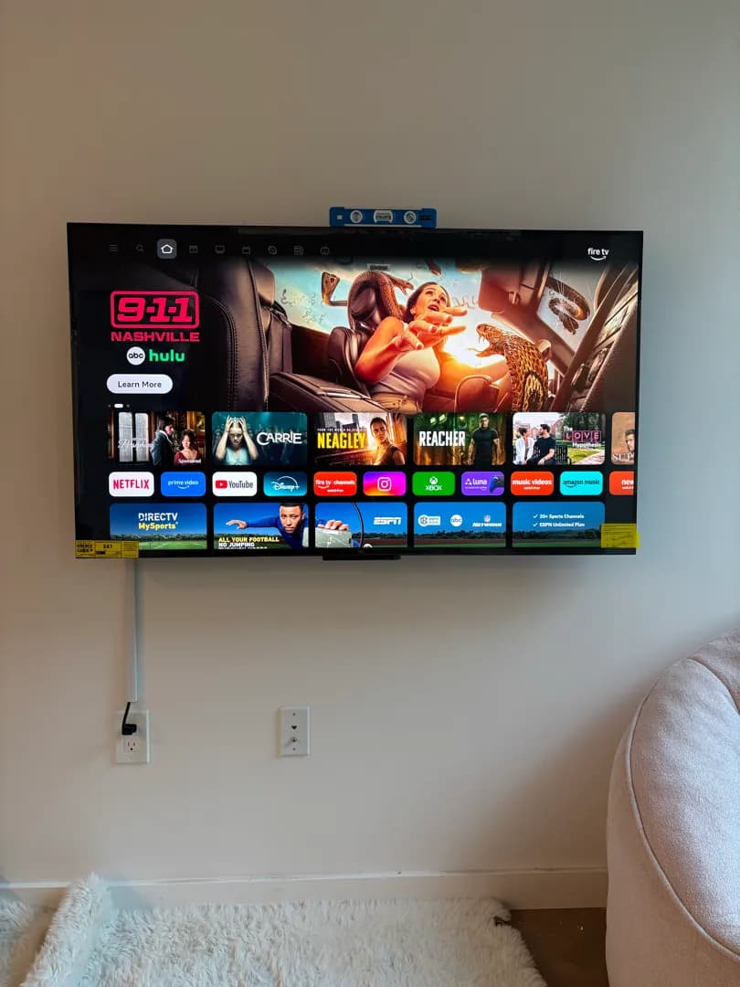 A 55-inch TV mounted flat on a plain wall with a small level resting on top and a white cord cover running down to an outlet.