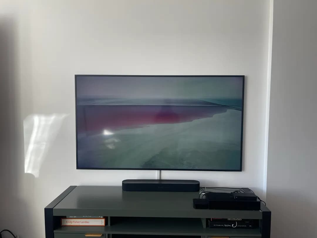 A slim Frame TV hanging flat on a white wall above a black soundbar on a green console.