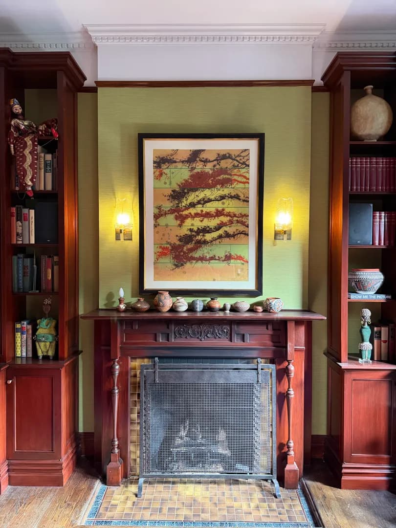 A fireplace with framed artwork above it and a small speaker visible on a bookshelf to the right.