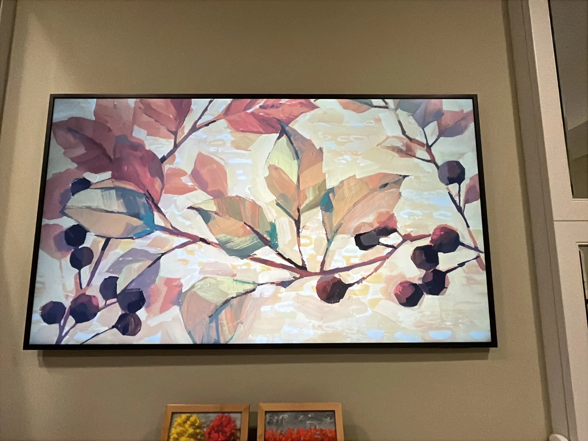A Frame TV in art mode displays a floral painting, mounted above a stone ledge holding two small framed paintings.